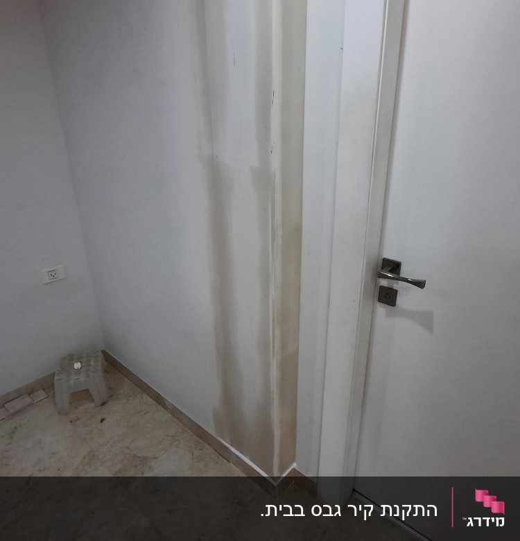 קיר גבס עם סימני רטיבות ליד דלת לבנה